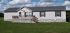 Gray Trailer Home With Stone Foundation Or Skirting And Shutters In Front Of A Beautiful Sky
