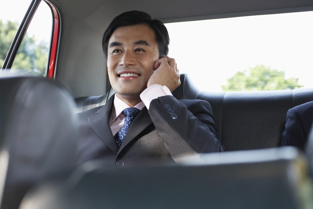 Happy young businessman using cellphone in backseat of car
