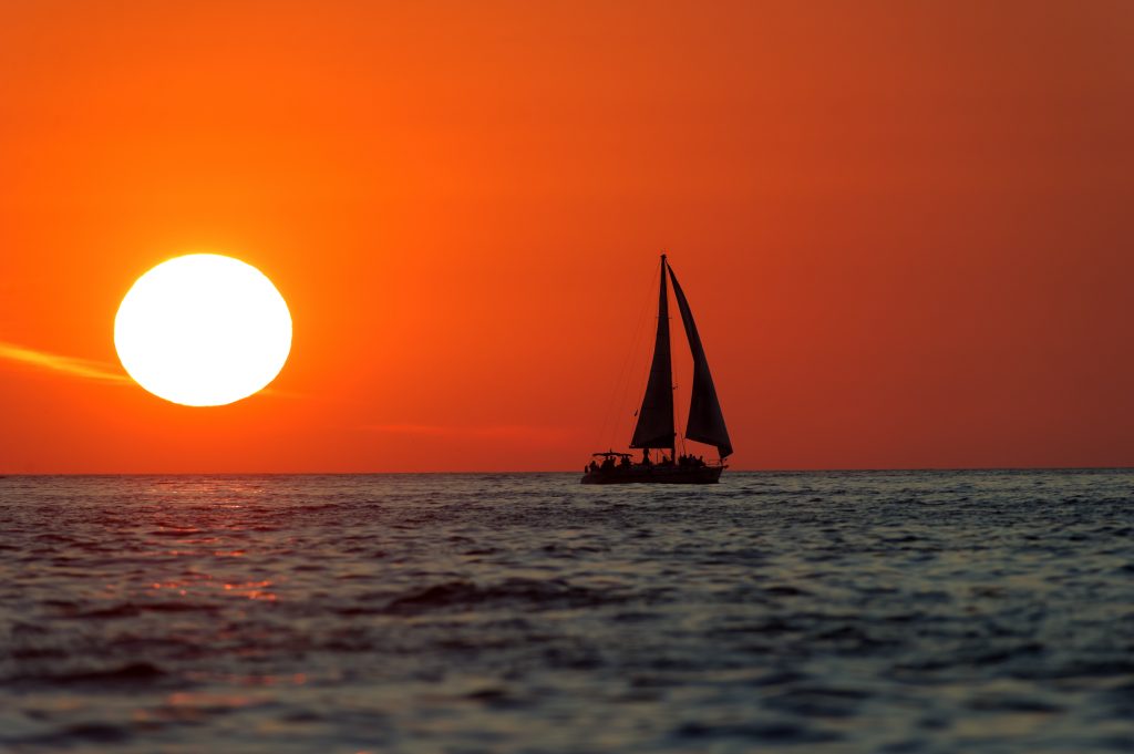 Sailboat Sunset is sailboat silhouetted a bright red sky with a bright white burning sun setting in the background